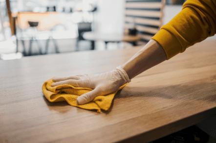 A person wiping a wooden table clean using a yellow cloth